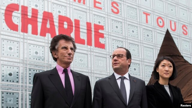 French President Francois Hollande, center, Culture Minister Fleur Pellerin, right, and Institut du Monde Arabe (Arab World Institute) President Jack Lang walk past the institute building, which bears the message "We are Charlie," in Paris, Jan. 15, 2015.