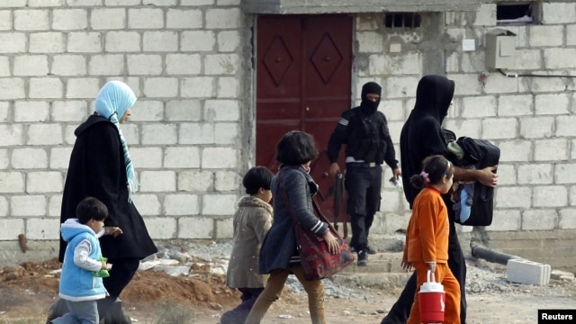 People from the northern Syrian town of Ras al-Ain attempt to cross into Turkey, as a Free Syrian Army fighter leaves a home in the background, as seen from the Turkish border town of Ceylanpinar, Sanliurfa province, November 13, 2012.