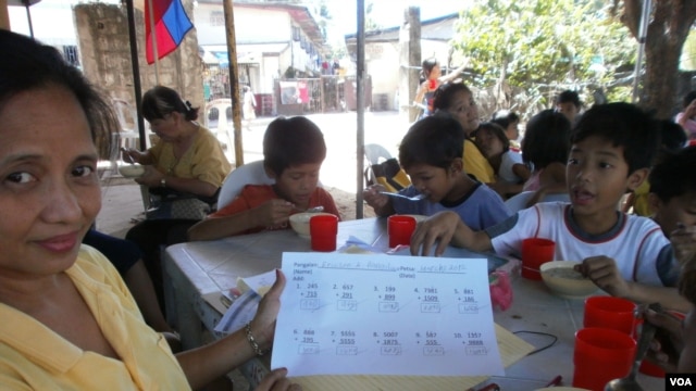 Lessons are over and a lunch of rice porridge with chicken and beans is served. Sitting at the 10-year olds' table, volunteer teacher Yolanda Penalosa shows off her student Ericson's quick progress in arithmetic, May 25, 2012. (S. Orendain/VOA)