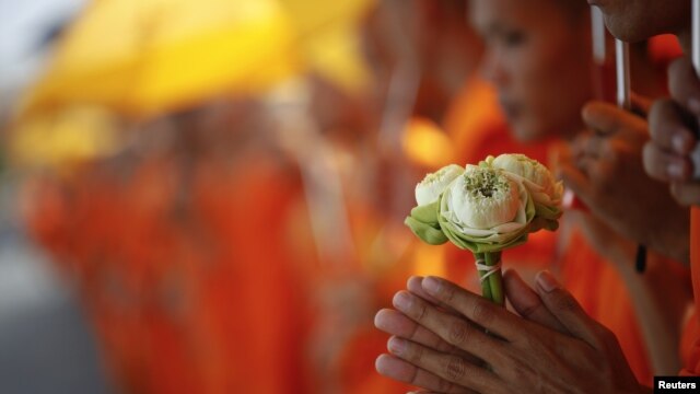 A Buddhist monk holds flowers as he joins others waiting for the coffin of the former king Norodom Sihanouk to arrive at the Royal Palace in Phnom Penh October 17, 2012. Tens of thousands poured into Cambodia's capital to witness the procession on Wednesday. 