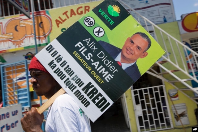 A supporter of the political party Platform Vérité carries a poster of parliamentary candidate Alix Didier Fils-Aime in Port-au-Prince, Haiti, Aug. 7, 2015.