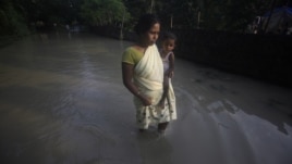A flood affected woman with her child wades through a flooded road in Chandrapur village, outskirts of Gauhati, Assam state, India, Sept. 25, 2012. 