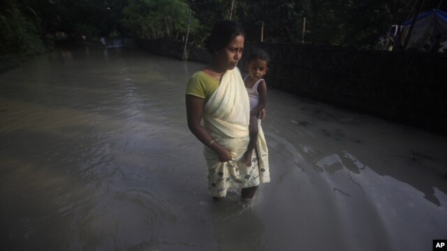 A flood affected woman with her child wades through a flooded road in Chandrapur village, outskirts of Gauhati, Assam state, India, Sept. 25, 2012. 