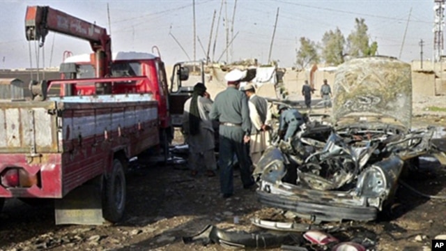 Afghan police inspect the wreckage of a car in which a district chief, his son and a bodyguard were killed by a car bomb in Kandahar, 15 June 2010