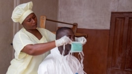 A healthcare worker, left,  helps a colleague as she prepares his Ebola personal protective equipment before entering the Ebola isolation ward at Kenema Government Hospital, in Sierra Leone, Aug. 12, 2014.