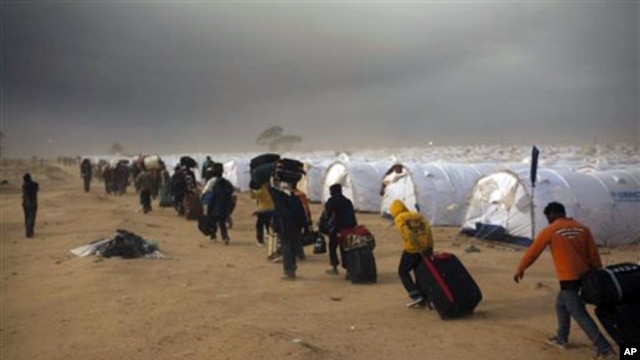 Men, who used to work in Libya and fled the unrest in the country, carry their belongings as they arrive during a sand storm in a refugee camp at the Tunisia-Libyan border, in Ras Ajdir, Tunisia, March 15, 2011