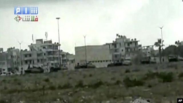 This image made from amateur video and released by Shams News Network and accessed via The Associated Press Television News on Saturday, Aug. 13, 2011, shows a long shot of military vehicles lined up on road, backdrop of buildings taking up positions near