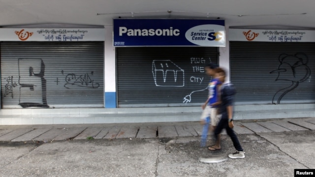 A couple walks past graffiti that reads "Plug The City." The phrase has appeared on various places in the capital, Rangoon, since the government implemented electricity cuts. 