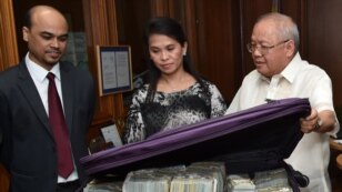 This photo provided by the Bangko Sentral ng Pilipinas, from left, Second Secretary and Head of Chancery of the Bangladesh Embassy in Manila Probash Lamarong, Anti-Money Laundering Council (AMLC) Secretariat Executive Director Julia Bacay-Abad and AMLC Member and Insurance Commissioner Emmanuel Dooc opens a bag containing US dollars that was returned by Chinese casino junket operator Kam Sin Wong to Bangladesh and Philippine AMLC officials in Manila, March 31, 2016. 