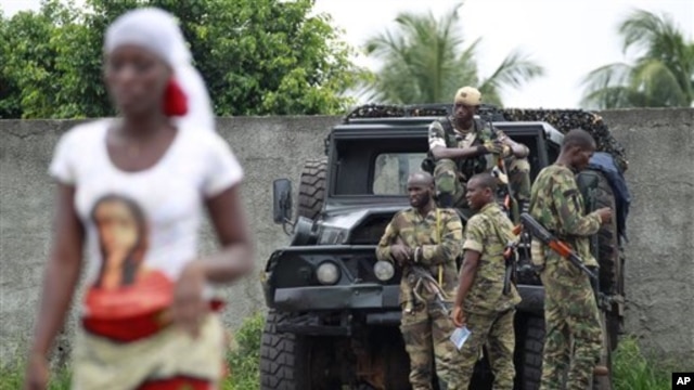 A woman walks past soldiers loyal to Alassane Ouattara as they man a checkpoint at one of the principal entrances to Abidjan, Ivory Coast, April 5, 2011