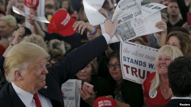 Ứng cử viên tổng thống của Đảng Cộng hòa Donald Trump cầm một tờ báo với tiêu đề "Clinton, Trump dẫn đầu" trong một buổi mít tinh ở  Warwick, Rhode Island, ngày 25 tháng 4 năm 2016. 