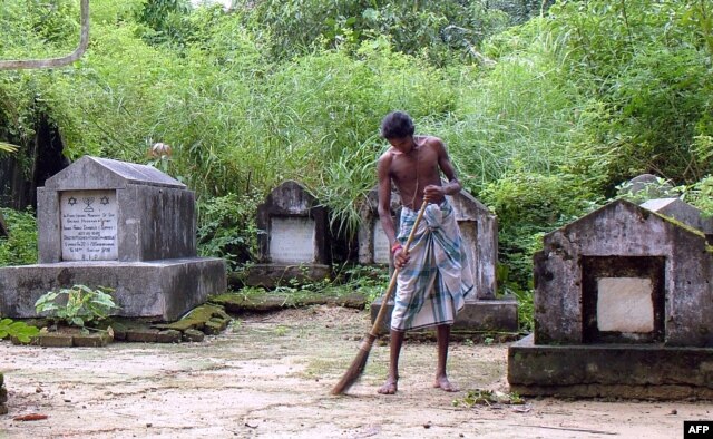 FILE - A worker cleans the ground near the graves at a Jewish cemetery located on the edge of Rangoon, Oct. 2006.