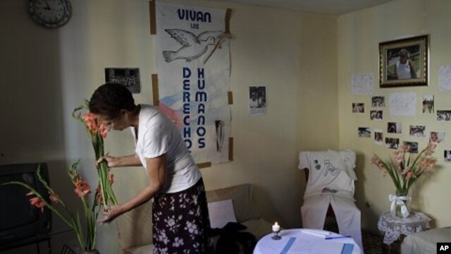 Ramona Rivero, of the Cuban dissident group Ladies in White, places flowers in a vase near a condolence book for the late dissident Wilman Villar in Havana, Cuba, Friday, Jan. 20, 2012.