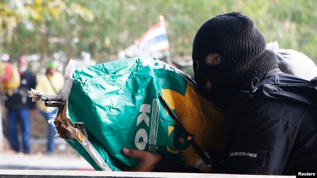 An anti-government protester shoots his rifle, hidden it inside a sack, toward pro-government protesters during clashes in Bangkok, Thailand, Feb. 1, 2014.