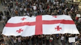 Georgian demonstrators carry a state flag during a protest rally against prison abuse in Tbilisi, Georgia, Sept. 20, 2012