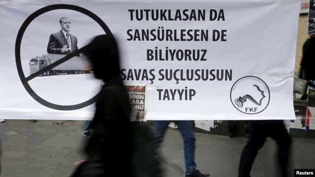 FILE - A woman walks past a banner picturing Turkish President Recep Tayyip Erdogan that reads, "When you arrest (journalists) or censor (media) we know that you are a war criminal, Tayyip," during a protest in Ankara, Turkey, Nov. 27, 2015.