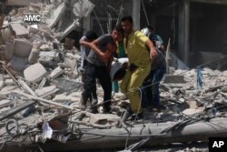 This photo provided by the Syrian anti-government activist group Aleppo Media Center (AMC), shows Syrians carrying a victim after barrel bombs were dropped on the Bab al-Nairab neighborhood in Aleppo, Syria, Aug. 27, 2016.