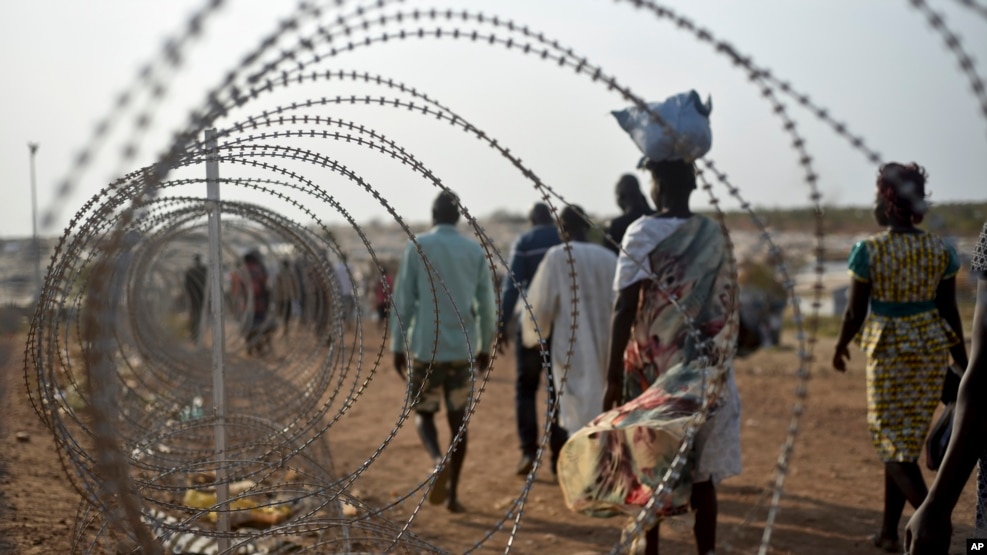 A file photo taken Jan. 19, 2016 shows displaced people walking next to a razor wire fence at the United Nations base in the capital Juba, South Sudan.