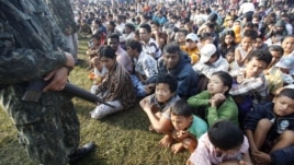 A Thai soldier stands guard as refugees from Burma sit at the Thai-Burma border town of Mae Sot, waiting to go to refugee camps in Thailand, November 9, 2010.