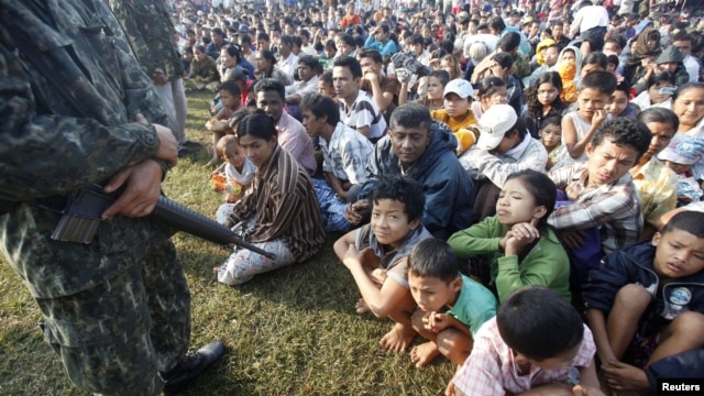 A Thai soldier stands guard as refugees from Burma sit at the Thai-Burma border town of Mae Sot, waiting to go to refugee camps in Thailand, November 9, 2010.