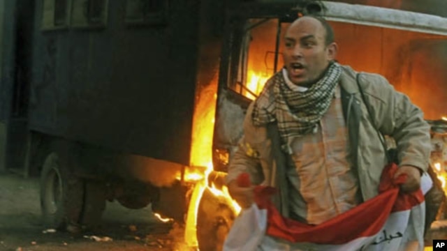 A protester holds an Egyptian flag next to a police vehicle that was set ablaze during clashes between protesters and security forces in Cairo, November 19, 2011.