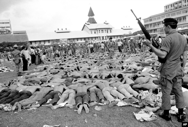 FILE - In this Oct. 6, 1976 file photo, police stand guard over leftist Thai students on a soccer field at Thammasat University, in Bangkok, Thailand. For some Thais, the bloody events of October 6, 1976 are still a nightmare. On that day, heavily armed s