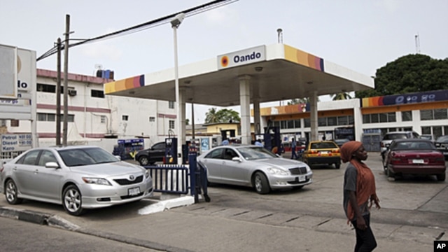 A woman walks past cars buying fuel at a gas station in Lagos, Nigeria, April 24, 2012.