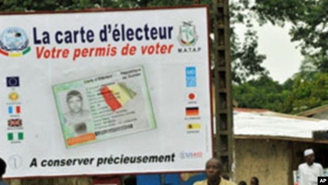 People walk in front of posters for the presidential elections and instructions on the voting card, Conakry, 25 Jun 2010