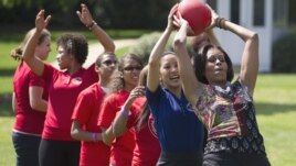 First lady Michelle Obama hands a ball to Olympic skater Michelle Kwan during an event in 2011 to promote physical fitness among military families
