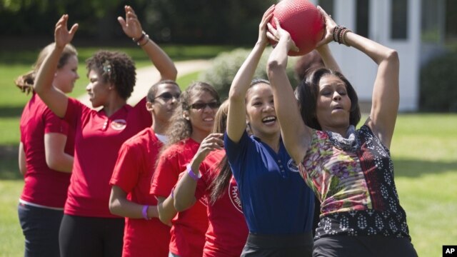 First lady Michelle Obama hands a ball to Olympic skater Michelle Kwan during an event in 2011 to promote physical fitness among military families