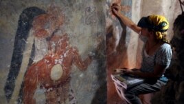 Conservator Angelyn Bass cleans and stabilizes the surface of a wall of a Maya house that dates to the 9th century A.D. The figure of a man who may have been the town scribe appears on the wall to her left. (Tyrone Turner © 2012 National Geographic)