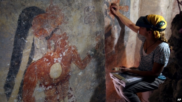 Conservator Angelyn Bass cleans and stabilizes the surface of a wall of a Maya house that dates to the 9th century A.D. The figure of a man who may have been the town scribe appears on the wall to her left. (Tyrone Turner © 2012 National Geographic)