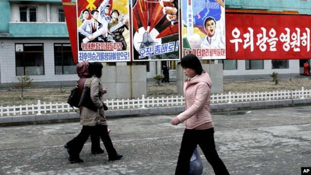 North Koreans walk past posters reading "Forward to the ultimate victory under the leadership of the great party!" on March 19, 2013 on a street in Phyongchon District in Pyongyang.