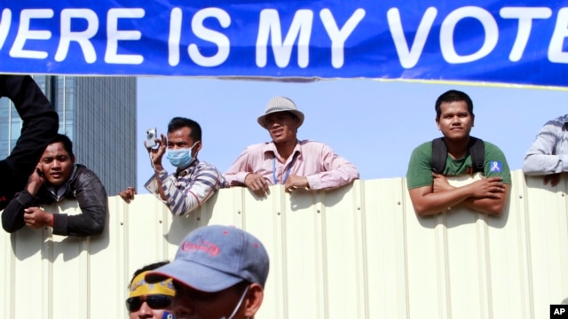 Cambodian workers look through a partition of a construction site below a banner which reads "Where is my vote" as supporters of opposition Cambodia National Rescue Party gather in Phnom Penh, file photo. 