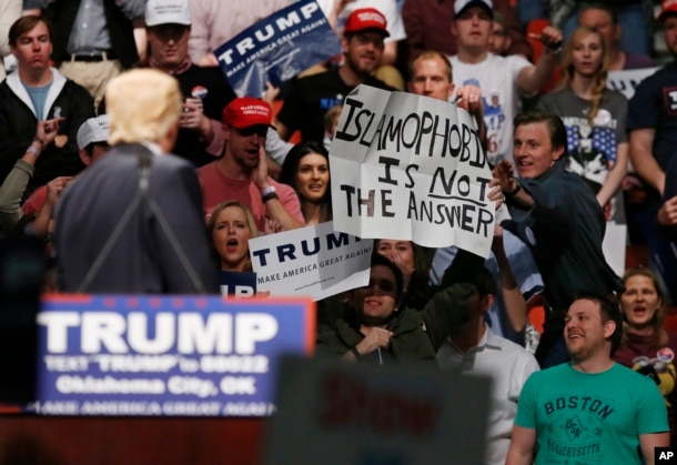 FILE - Republican presidential candidate Donald Trump, left, looks on as one of his supporter reaches for a sign that reads "Islamophobia is not the answer," at a rally in Oklahoma City, Feb. 26, 2016.