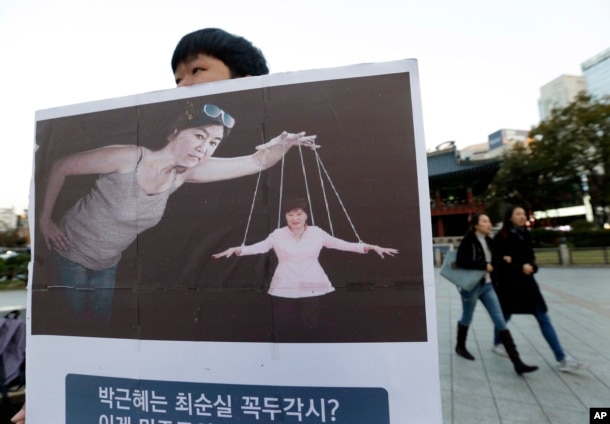 A South Korean college student holds a placard depicting South Korea's President Park Geun-hye, right bottom, as a marionette and Choi Soon-sil, who is at the center of a political scandal, as a puppeteer, in Seoul, South Korea, Nov. 3, 2016.