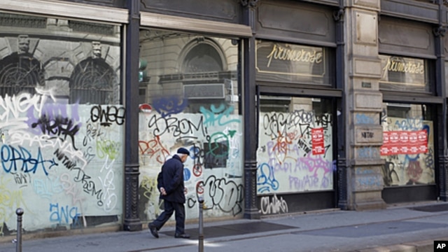 A man walks next to the windows of a closed shop in downtown Milan, Italy, April 12, 2012. 