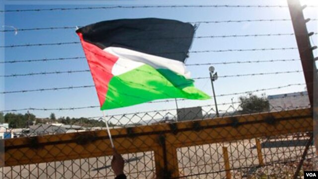 Seorang warga Tepi Barat mengibarkan bendera Palestina di pos pemeriksaan Beituniya (Foto: dok). Militer Israel dilaporkan menembak mati seorang remaja Palestina di dekat tembok pemisah Tepi Barat. 