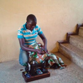 'Mobile tailor' Abubakar Mohammed sews outside a home, as he travels door-to-door with his sewing machine on his shoulder looking for work, in the capital, Abuja, Nigeria, February 15, 2012.