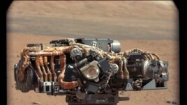 This image shows the Mars Hand Lens Imager (MAHLI) on NASA's Curiosity rover, with the Martian landscape in the background. Image was taken by Curiosity's Mast Camera, Sept. 8, 2012, UTC). (NASA/JPL-Caltech/MSSS)