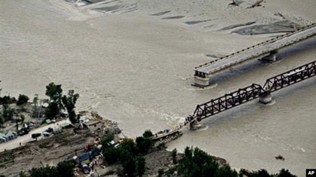 Flood survivors cross a hastily-repaired bridge next to a main bridge swept away by flood waters in Swat Valley, 10 Aug 2010