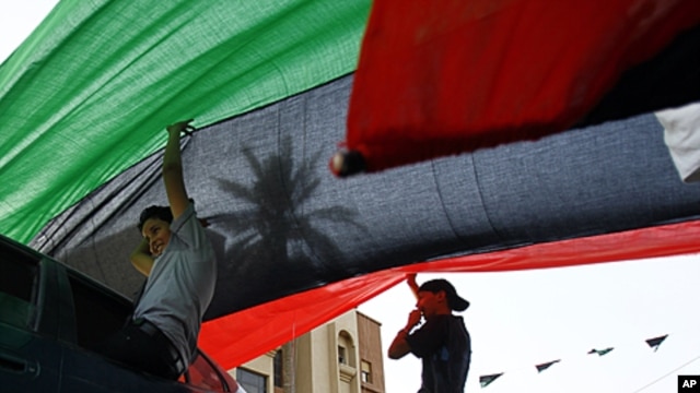 Libyan residents of Jamal Goubtan district in Tripoli hold a giant former Libyan flag for the cars driving under in the streets of Tripoli, Libya, Sept. 1, 2011
