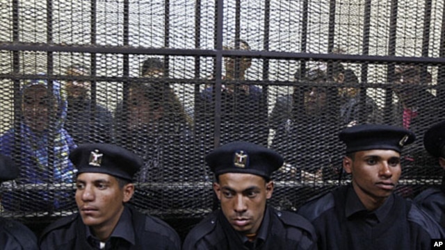 Policemen sit in front of a cage holding Egyptian employees of several pro-democracy groups during court proceedings in Cairo, Egypt, Sunday, February 26, 2012.