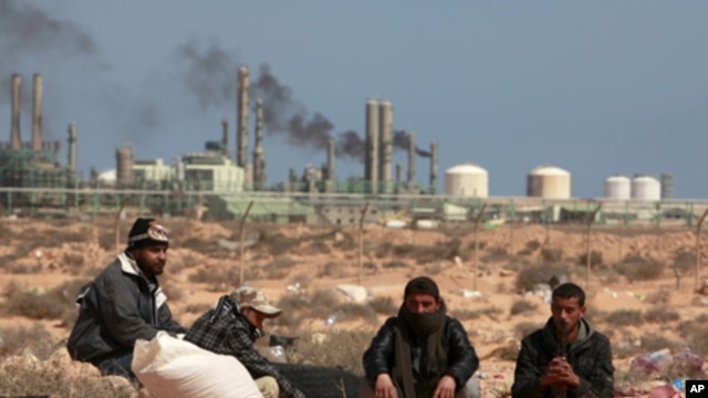 Anti-Gaddafi rebels sit on the ground near an oil facility in Ras Lanuf, March 10, 2011. The rebel leadership said on Thursday that the oil port of Ras Lanuf in eastern Libya is under heavy bombardment.
