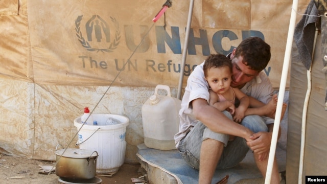 A Syrian refugee holds his child as he sits by his tent at Al Zaatri refugee camp in the Jordanian city of Mafraq, near the border with Syria, Sept. 9, 2012. 