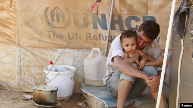 A Syrian refugee holds his child as he sits by his tent at Al Zaatri refugee camp in the Jordanian city of Mafraq, near the border with Syria, September 9, 2012. 