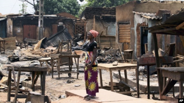 A woman stands in front of burnt buildings in Kachia village, where violence erupted last week, in Nigeria's northern state of Kaduna, April 28, 2011