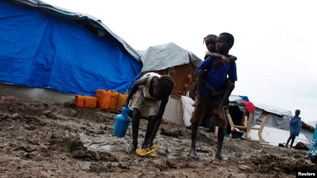 FILE - A boy carries a girl as they walk through the mud in an internally displaced persons (IDP) camp inside the U.N. base in Malakal, South Sudan, July 24, 2014.