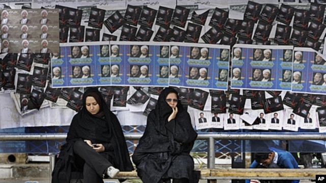 Iranian women sit at bus stop, in front of parliamentary elections campaign posters in the city of Qom, 78 miles (125 kilometers) south of the capital Tehran, March 1, 2012.