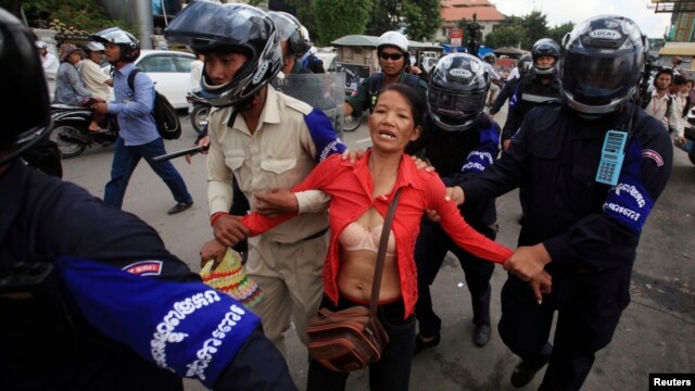 A protester is detained by Cambodian police officers during a rally in support of seven detained activists, in front of the Phnom Penh Municipal Court, in Phnom Penh, Nov. 11, 2014.